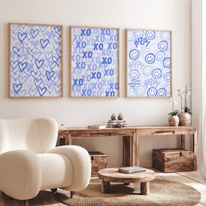 Peut inclure: Trois impressions d'art encadr&eacute;es avec des motifs bleu clair. L'une pr&eacute;sente des c&oelig;urs bleus, une autre le texte "XO", et la troisi&egrave;me des &eacute;motic&ocirc;nes souriantes et le mot "HAPPY". Les impressions sont dans des cadres en bois, au-dessus d'une console en bois.