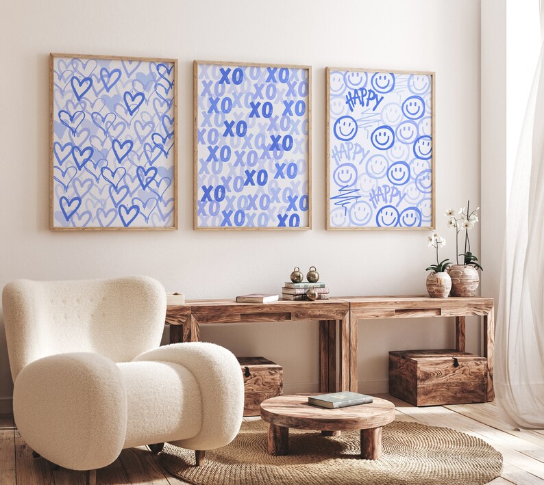 Peut inclure: Trois impressions d'art encadr&eacute;es avec des motifs bleu clair. L'une pr&eacute;sente des c&oelig;urs bleus, une autre le texte "XO", et la troisi&egrave;me des &eacute;motic&ocirc;nes souriantes et le mot "HAPPY". Les impressions sont dans des cadres en bois, au-dessus d'une console en bois.