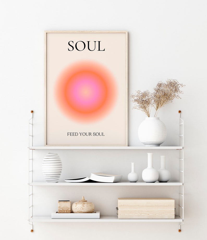 May include: A framed art print with the word "SOUL" at the top and "FEED YOUR SOUL" at the bottom. The artwork features a gradient circle in shades of pink and orange. The print is displayed on a white shelf with decorative vases and a wooden box.