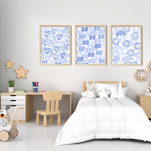 Peut inclure: Trois impressions d'art encadr&eacute;es avec des motifs bleus sont accroch&eacute;es au-dessus d'un lit d'enfant. Les impressions pr&eacute;sentent des c&oelig;urs, du texte "XO" et des visages souriants avec le mot "Happy". La chambre a un bureau, une chaise et une poussette jouet.
