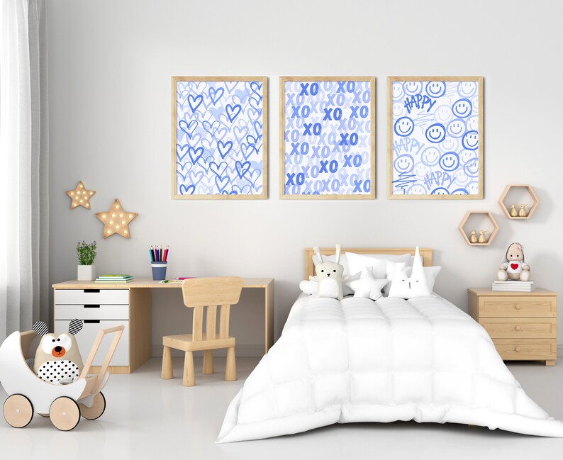 Peut inclure: Trois impressions d'art encadr&eacute;es avec des motifs bleus sont accroch&eacute;es au-dessus d'un lit d'enfant. Les impressions pr&eacute;sentent des c&oelig;urs, du texte "XO" et des visages souriants avec le mot "Happy". La chambre a un bureau, une chaise et une poussette jouet.