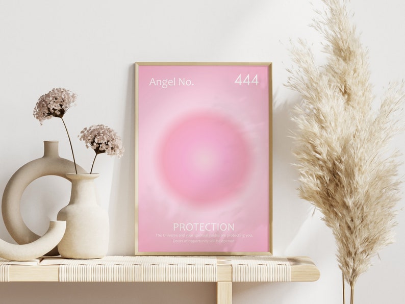 May include: A framed poster with a pink background and a white circle in the center. The poster has the text "Angel No. 444" at the top and "PROTECTION" at the bottom. The text below "PROTECTION" reads "The universe and your guardian angels are always sending you positive support and love to help you."
