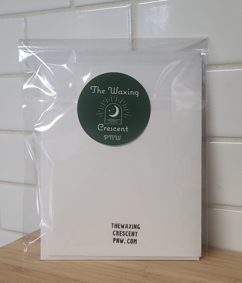Może przedstawiać: Biała kartka z zieloną okrągłą naklejką. Naklejka przedstawia rosnący księżyc i gwiazdy z tekstem "The Waxing Crescent PNW" w kolorze białym. Na dole kartki znajduje się tekst "THE WAXING CRESCENT PNW.COM" w kolorze czarnym.