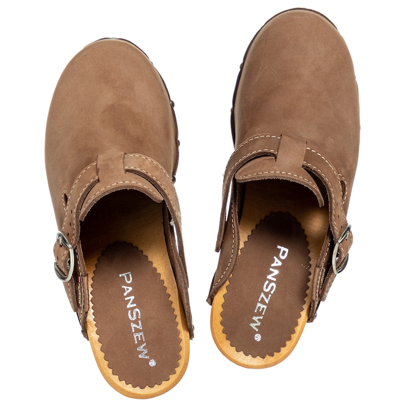 May include: A pair of brown leather clogs with a buckle strap. The clogs have a wooden sole with the brand name "PANSZEW" printed on the insole.