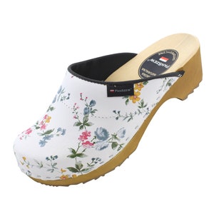 Könnte beinhalten: Weiße Clogs mit Blumenmuster und Holzabsatz. Die Clogs haben eine schwarze Innensohle und eine braune Sohle. Der Markenname "PANSZIEW" ist an der Seite des Clogs aufgedruckt.