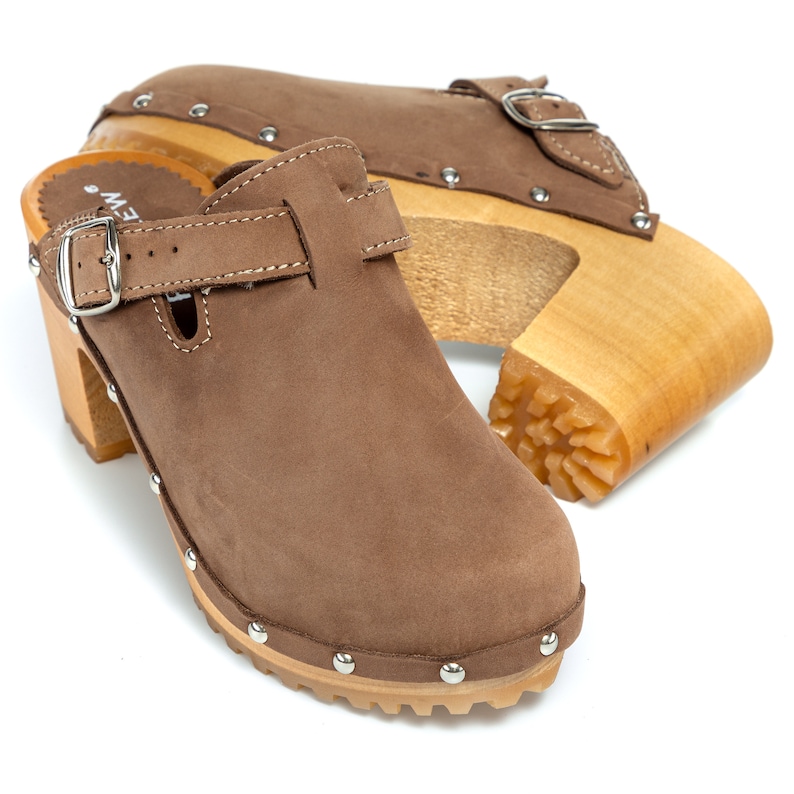 May include: A pair of brown suede clogs with wooden heels and a buckle closure. The clogs have a studded design around the sole and heel.