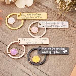 May include: Four keychains with different messages on them. The keychains are gold, silver, rose gold, and black. Each keychain has a small smiley face charm. The messages on the keychains are: "Drive safe handsome. I need you here with me", "Drive safe. Have fun. Don't do stupid shit", "To the best mom in the world. Rebekah & Jackie", and "You are the greatest catch of my life".