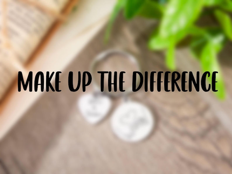 May include: A silver-toned metal keychain featuring a circular ring, a heart-shaped charm, and a circular charm. The text "MAKE UP THE DIFFERENCE" is prominently displayed in black lettering across the center of the image over the charms.