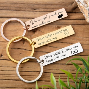 May include: Three gold keychains with silver rings. Each keychain has a rectangular tag with a message: "Drive safe! I need you here with me". The first tag has two hearts, the second has one heart, and the third has an infinity symbol.