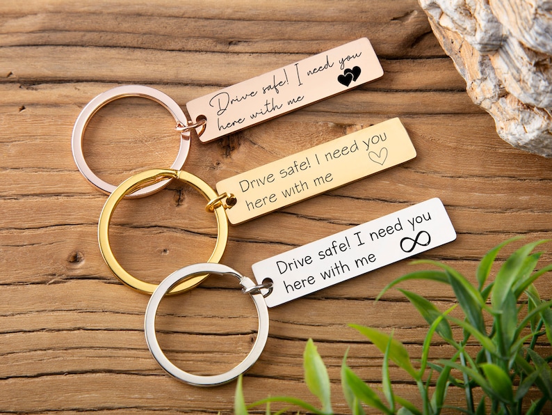 May include: Three gold keychains with silver rings. Each keychain has a rectangular tag with a message: "Drive safe! I need you here with me". The first tag has two hearts, the second has one heart, and the third has an infinity symbol.