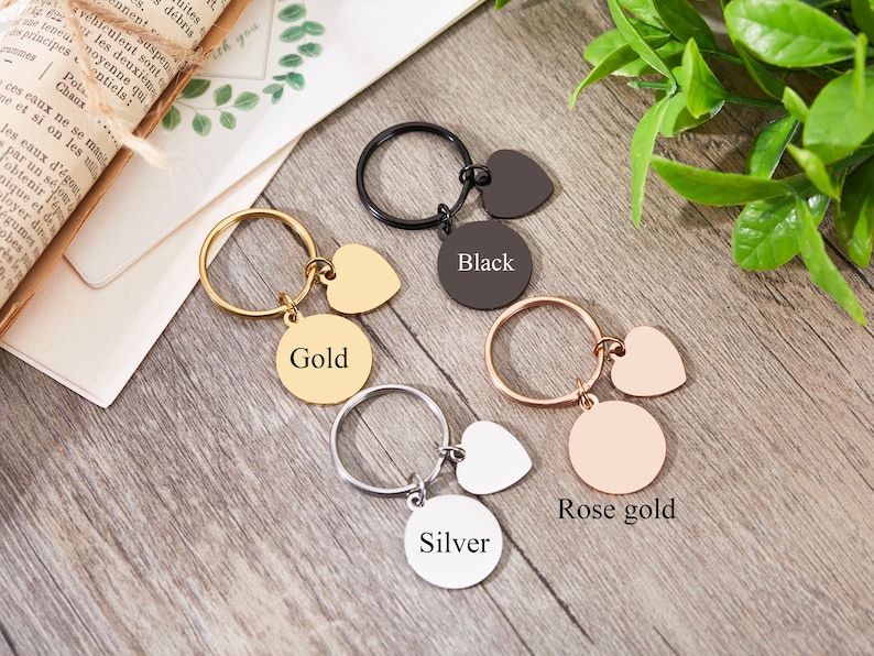 May include: Four keychains with different colored metal finishes: gold, black, rose gold, and silver. Each keychain has a round charm with the color name and a heart-shaped charm.