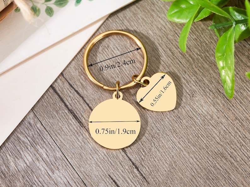 May include: Gold-toned keychain with a round charm measuring 0.75 inches in diameter and a heart-shaped charm measuring 0.55 inches in width. Both charms have engraved measurements in inches and centimeters.
