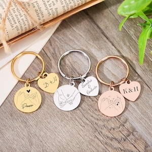 May include: Three gold, silver, and rose gold keychains with heart-shaped charms and round charms featuring a pinky promise design. The charms are engraved with the names "D+H", "Sandra & Godwin", and "K&H".