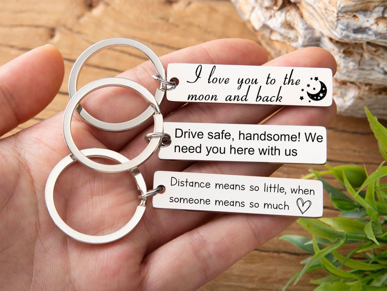 May include: Silver keychain with three rings and three rectangular tags. The tags have the following text: "I love you to the moon and back", "Drive safe, handsome! We need you here with us", and "Distance means so little, when someone means so much".