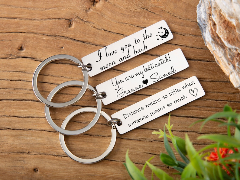 May include: Three silver keychains with engraved messages. The top keychain says "I love you to the moon and back". The middle keychain says "You are my best catch! Gianna Samuel". The bottom keychain says "Distance means so little, when someone means so much".