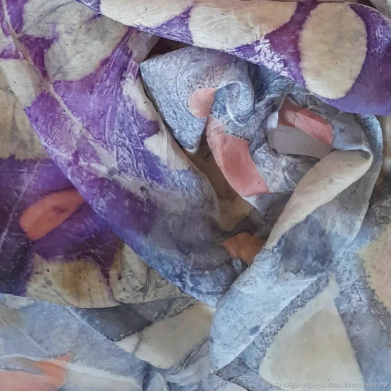 Op de afbeelding: Een zijden sjaal met een handgeschilderd ontwerp in tinten paars, roze en grijs. De sjaal is gemaakt van een zachte, vloeiende stof en heeft een uniek, abstract patroon.