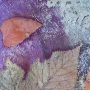 Op de afbeelding: Een close-up van een textuurrijke achtergrond in paars en wit met geperste bladeren in tinten bruin en oranje.