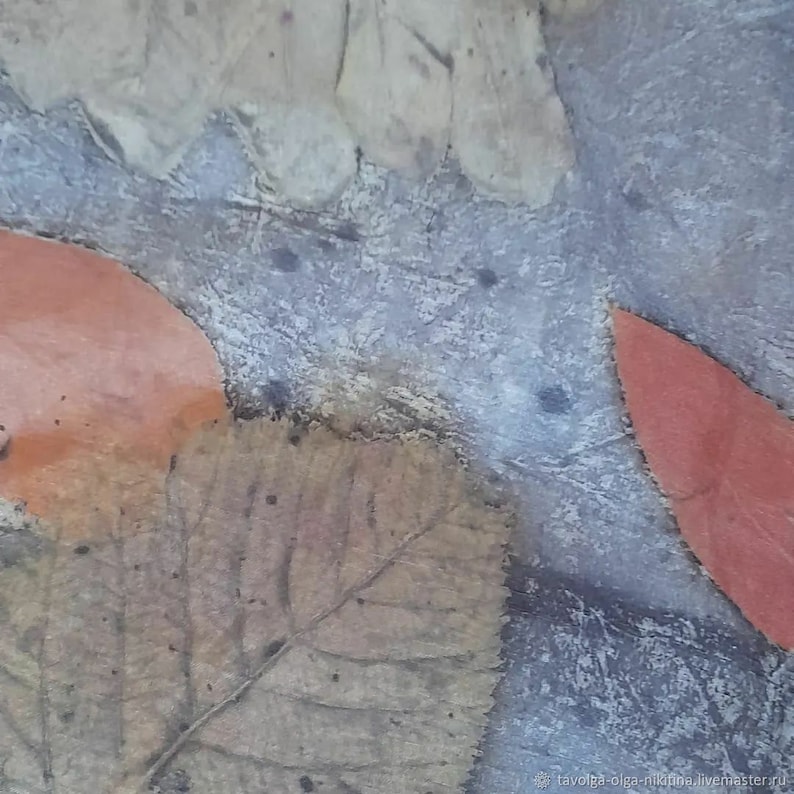 Op de afbeelding: Een close-up van een textuurrijke, grijze achtergrond met twee oranje bladeren en &eacute;&eacute;n bruin blad. De bladeren zijn in de achtergrond geperst en hebben een natuurlijke, organische uitstraling.