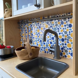 May include: A toy kitchen playset featuring a grey sink and a silver tap. The sink is made of plastic and has a white worktop. The tap has a single handle and a spout that extends over the sink. The worktop is decorated with a colourful tile pattern.