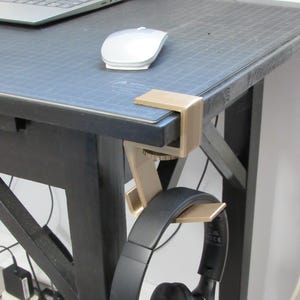 May include: A gold metal desk headphone holder with a black pair of headphones hanging from it. The headphones are labeled "KVIDIO".