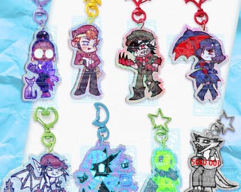 May include: Eight acrylic keychains featuring various illustrated characters with colorful clasps in shapes like hearts, stars, bats, and moons. The characters include figures in red, purple, green, and black outfits, with one keychain marked as sold out.