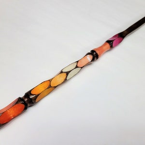 May include: A wooden wand with a pointed tip and a decorative design of overlapping orange, yellow, white, and pink ovals.