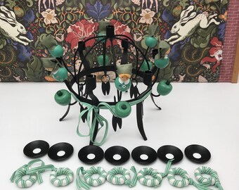 Puede incluir: Un candelabro de metal negro con detalles turquesa y una cinta turquesa. El candelabro tiene pequeñas figuras y esferas turquesas. También hay seis candelabros negros y cinco anillos decorativos a rayas turquesas y blancas.