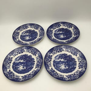 May include: Four blue and white decorative plates. Each plate features a scenic landscape design in the center, surrounded by a floral border. The plates are arranged on a white surface.