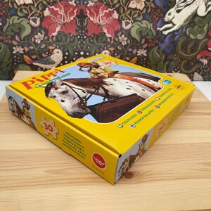 May include: A yellow square box for a 30-piece wooden puzzle featuring Pippi Longstocking riding a white horse with brown spots. The box lid displays the title Pippi L&aring;ngstrump, the number 30, and the Egmont logo, with text in multiple languages.