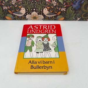 Può includere: Un libro con copertina rigida intitolato "Alla vi barn i Bullerbyn" di Astrid Lindgren. La copertina presenta illustrazioni di bambini ed è ambientata su uno sfondo rosso, blu e giallo. Il libro è in buone condizioni.