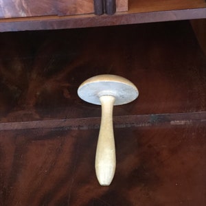 Może przedstawiać: Biała drewniana forma do kapelusza z okrągłym wierzchołkiem i długim, smukłym trzonem. Forma stoi na ciemnobrązowej drewnianej powierzchni.