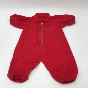 Op de afbeelding: Een rode baby romper met een rits aan de voorkant en een klein zakje op de borst.