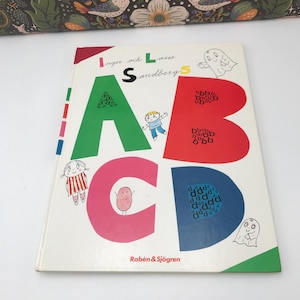以下が含まれることがあります： カラフルな大きな文字でA、B、C、Dの文字が書かれた子供向けの絵本表紙。文字は同じ色の小さな文字でいっぱいになっています。本のタイトルは「Inger och Lasse Sandberg」、出版社は「Rabén & Sjögren」です。