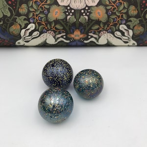 Peut inclure: Trois billes en verre avec une finition irisée mouchetée. Les billes sont bleues, vertes et noires avec des reflets dorés.