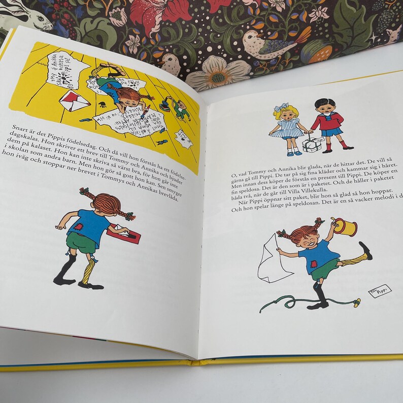 May include: Open book with colorful illustrations from a children's story. The pages feature drawings of children, text, and a yellow background. The book is open to a double-page spread with text in Swedish.