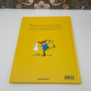 May include: A yellow children's book with the title "Pippi Longstocking" in Swedish. The back cover features an illustration of Pippi and the publisher's logo. The book is a children's storybook.