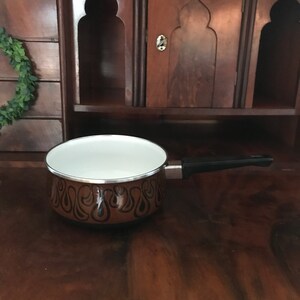 May include: A brown and black enamel saucepan with a white interior and a black handle. The saucepan has a paisley pattern.