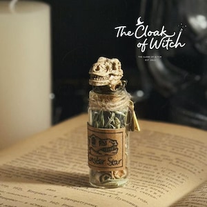 May include: A small glass bottle with a cork stopper topped by a miniature dinosaur skull. The bottle contains dried green herbs and features a tan paper label with a dinosaur skull illustration and the text Monster Star printed on the front.