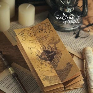 May include: A detailed, aged parchment map with the text "Marauder's Map" and other inscriptions. The map is folded and surrounded by other aged papers, a wand, and a magnifying glass. The words "The Cloak of Witch" are also visible.