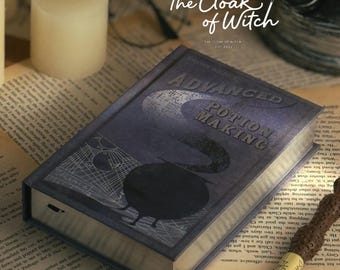 May include: A rectangular book titled Advanced Potion Making with a dark blue cover featuring a black cauldron graphic, geometric lines, and a crescent moon shape. A brown textured wand with a light-colored handle rests diagonally across the book.