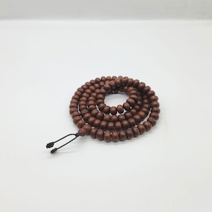 May include: A brown wooden mala bead necklace with a black cord. The beads are round and have a slightly textured surface.