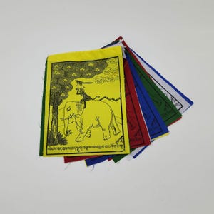 以下が含まれることがあります： カラフルな祈りの旗のコレクション。メインの旗は黄色で、象に乗る人の黒いイラストが描かれています。他の旗は赤、青、緑、白です。各旗には外国語のテキストがあります。