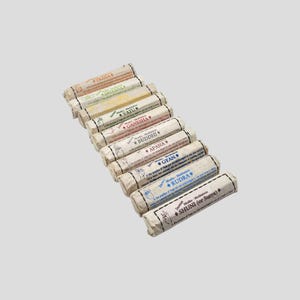 Può includere: Un assortimento di bastoncini di incenso, ciascuno avvolto in carta con etichette di vari colori. Le etichette presentano testi come "Prana", "Dhyana" e "Ganesha", insieme a illustrazioni di gesti delle mani. I bastoncini di incenso sono disposti in diagonale.