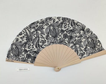 Op de afbeelding: Een vouwbare handwaaier met een lichtgekleurd houten frame en een stoffen blad met een zwart-witte botanische print van diverse bladeren en planten. De tekst "mimi coton" staat op het houten frame en op een klein wit rechthoekig label.