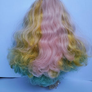 May include: A long, wavy wig with three sections of hair: yellow, pink, and teal. The wig is styled in a loose, flowing style.