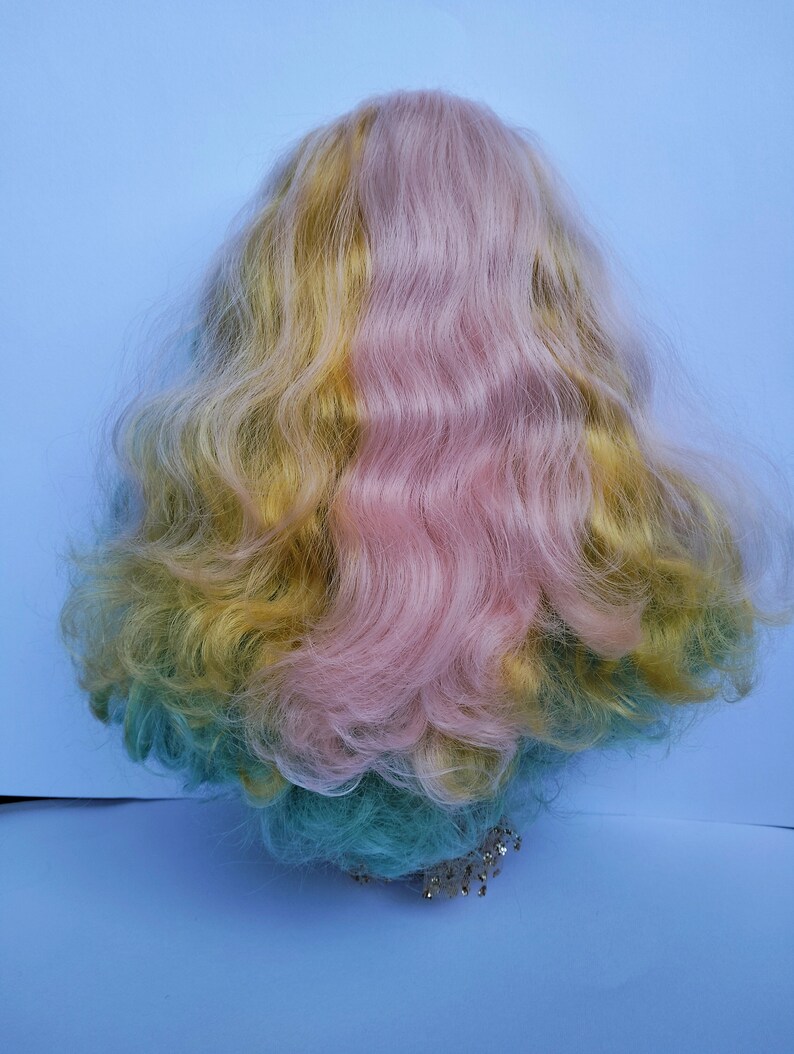 May include: A long, wavy wig with three sections of hair: yellow, pink, and teal. The wig is styled in a loose, flowing style.