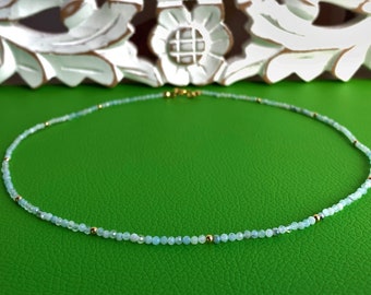 May include: A delicate necklace made of light blue beads with gold accents. The necklace is on a green background.