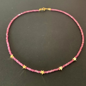 May include: A pink gemstone necklace with gold star accents. The necklace is made of small, faceted beads and has a delicate, feminine look.