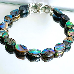 Peut inclure: Un bracelet en chaîne argent avec des perles ovales en nacre d'ormeau. Les perles sont irisées de vert, de bleu et de brun.