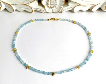 May include: A delicate blue gemstone necklace with gold star accents. The necklace is made of small, round beads and features a simple, elegant design.
